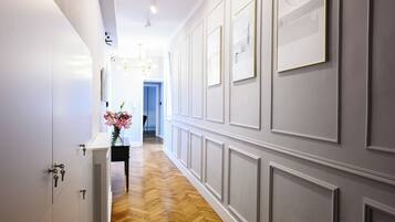 A hallway with white walls, wooden flooring, and a black table with a vase of flowers.