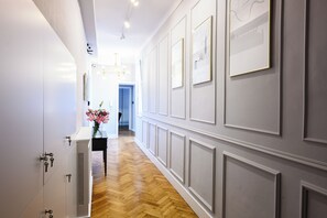 A hallway with white walls, wooden flooring, and a black table with a vase of flowers. - Wiślna Main Square Apartments Self Check-in (Kraków)