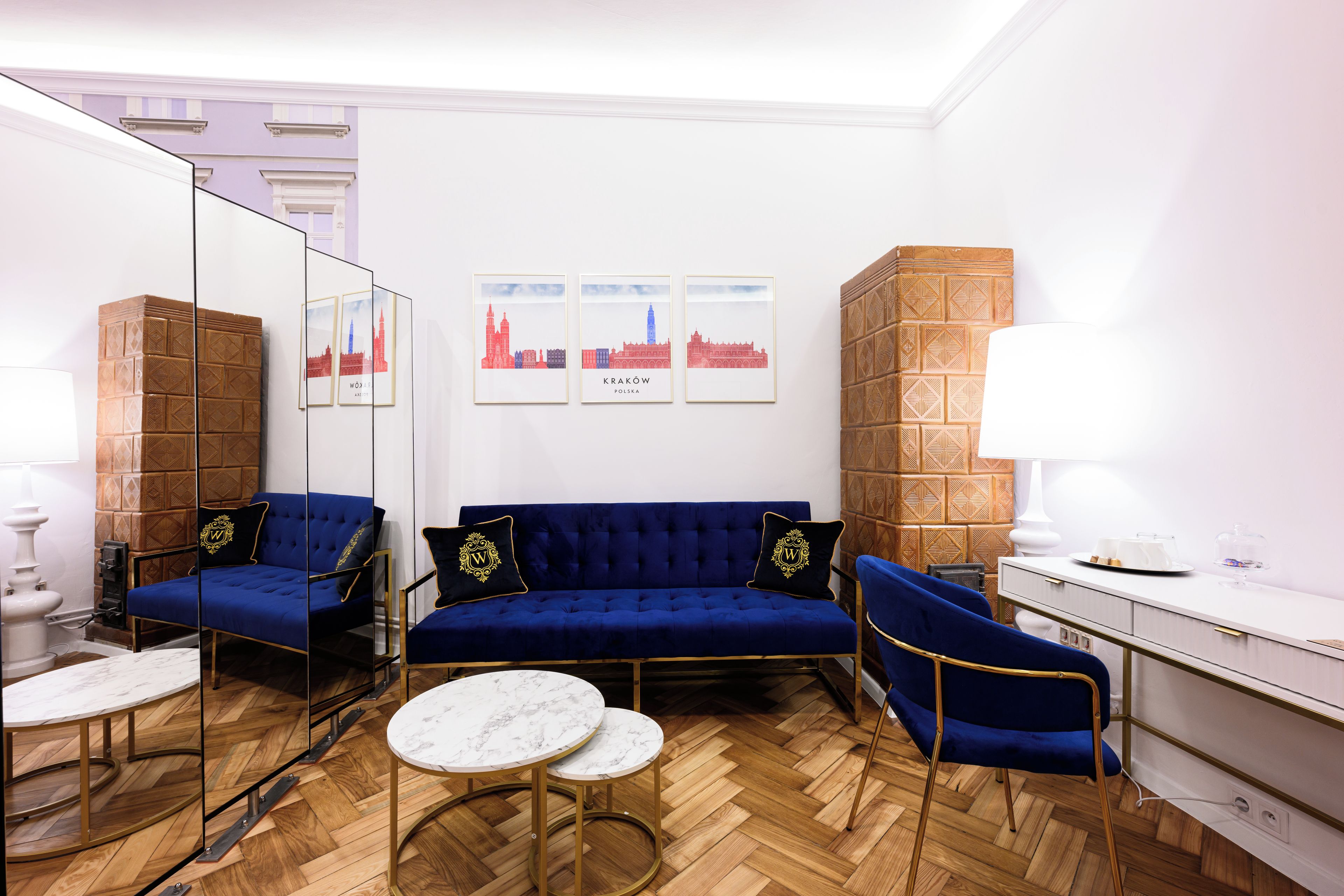A room with a blue sofa, a white desk, a mirror, and three framed pictures on the wall.