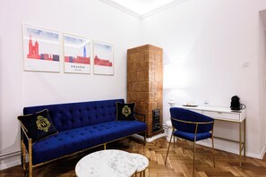 A room with a blue sofa, a white coffee table, a blue chair, a white desk, and a brick fireplace. There are three framed pictures on the wall. - Wiślna Main Square Apartments Self Check-in (Kraków)