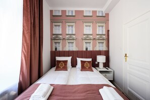 A double bed with two pillows, a nightstand with a lamp, and a view of a building facade through the window. - Wiślna Main Square Apartments Self Check-in (Kraków)