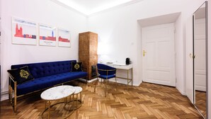 Un soggiorno moderno con un divano blu, un tavolino da caffè bianco e un pavimento in legno a spina di pesce. Si vedono quadri appesi al muro e un'imponente colonna con una superficie strutturata.