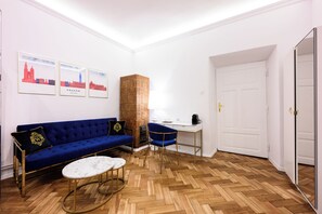 A modern living room with a blue sofa, a white coffee table, and a herringbone wooden floor. There are framed pictures on the wall and a tall, textured column. - Wiślna Main Square Apartments Self Check-in (Kraków)