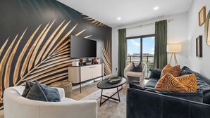 Una sala de estar moderna con sofá, sillón, mesa de centro, zona de cocina y un amplio ventanal con cortinas.