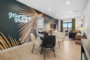 Une chambre d’hôtel moderne avec un coin repas, une grande fenêtre et un panneau lumineux au néon sur le mur.