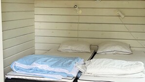 A small, single-room accommodation with two beds, a shelf with pictures, and a light fixture.
