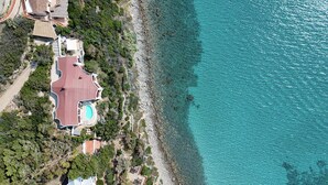 Oversigtsbillede af en ejendom ved kysten med swimmingpool, tennisbane og en bygning med rødt tag.