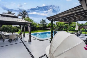 A pool area with a pergola, lounge chairs, and a covered seating area.