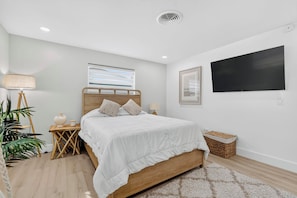 A modern bedroom with a wooden bed, a bedside table, a floor lamp, a potted plant, and a large window.