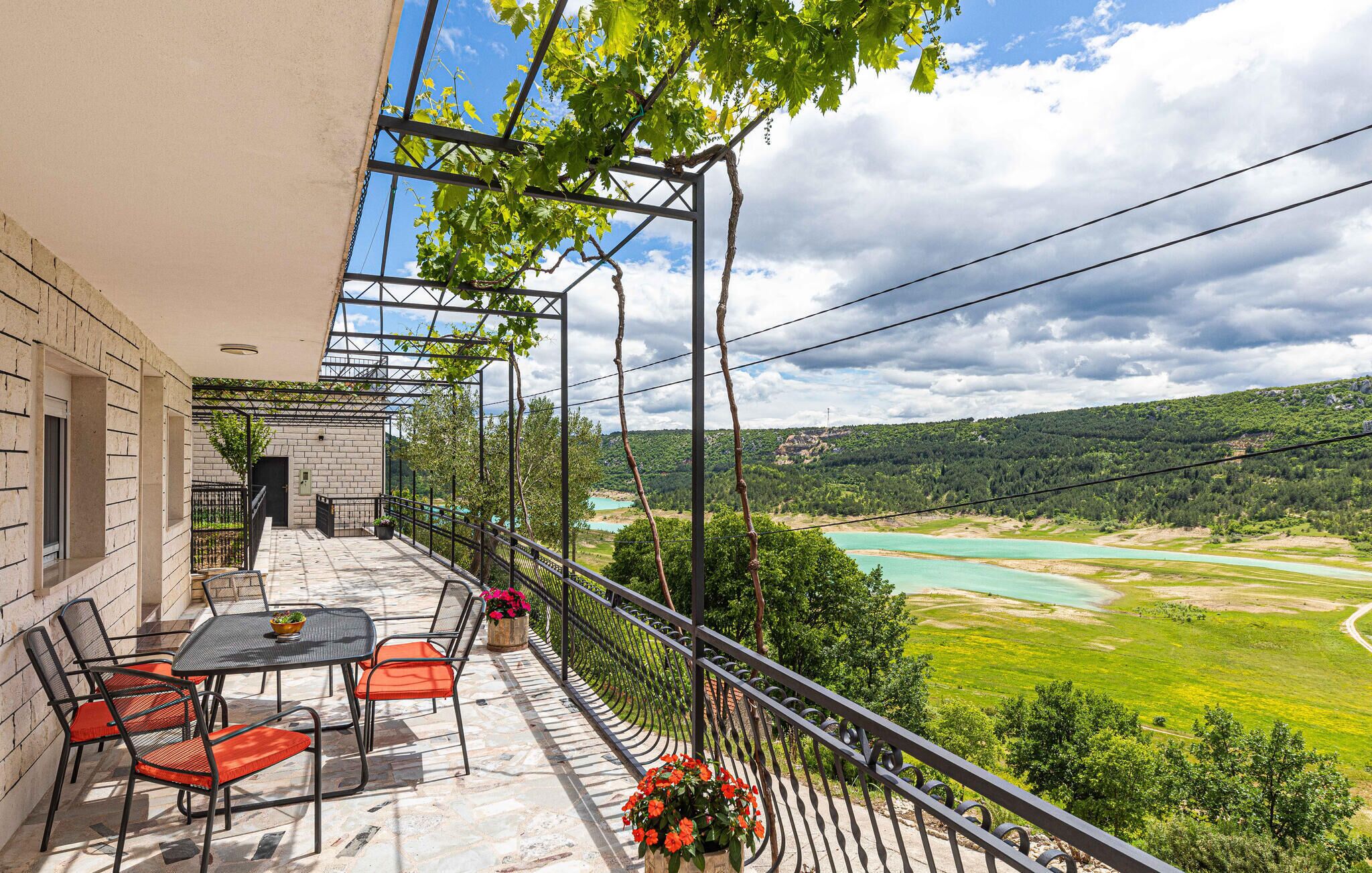 A balcony with a table and chairs, overlooking a river and green landscape.