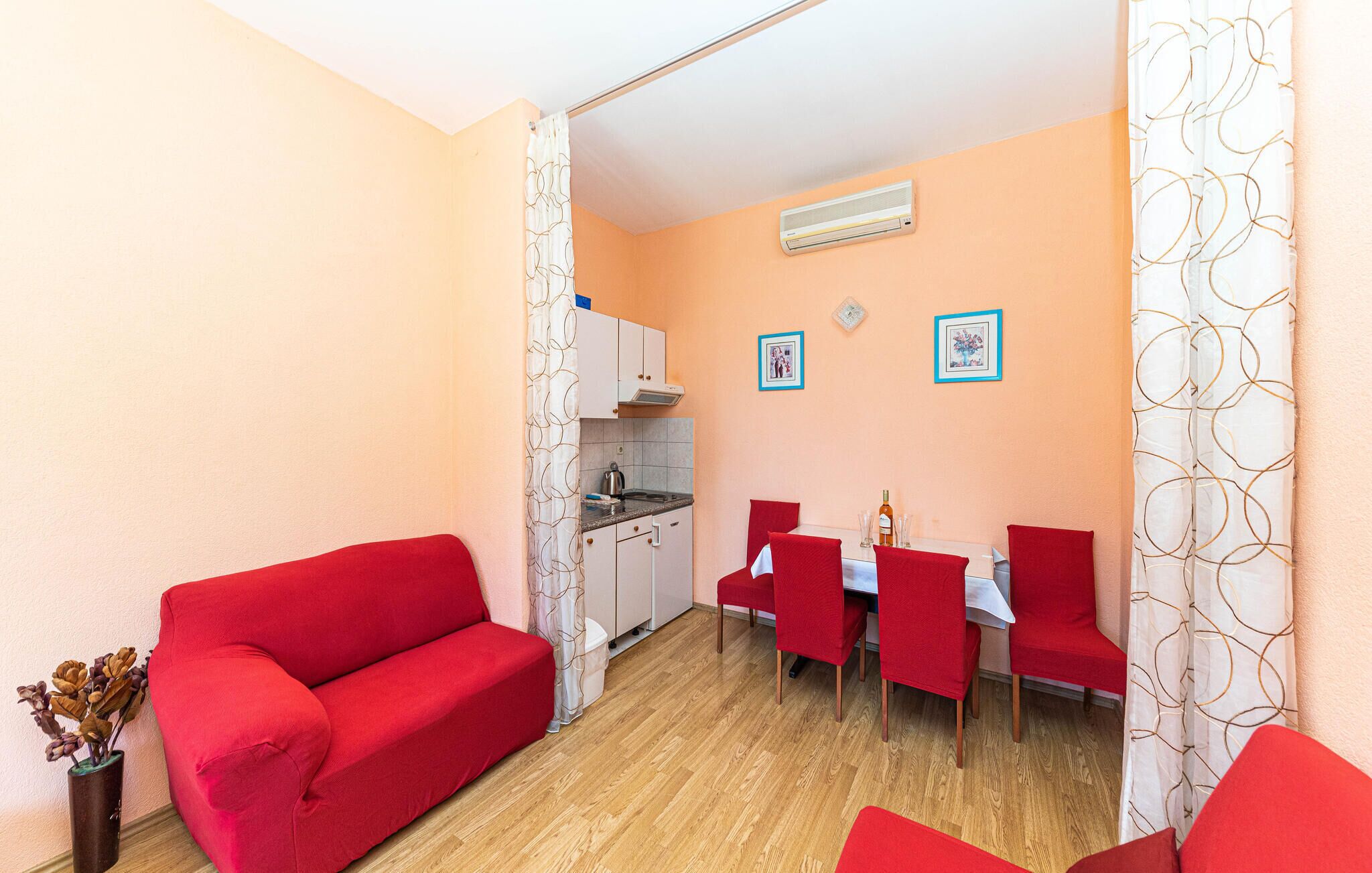 A compact living space with a kitchenette, a dining area with red chairs, and a red sofa.