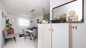 Un comedor moderno con una mesa blanca y sillas grises, un mueble blanco con espejo, y una planta encima.