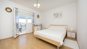 Un dormitorio con cama, mesitas de noche, escritorio, silla, armario y una puerta que da a un balcón con toldo a rayas.