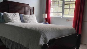 A bedroom with a bed, a nightstand, a window with curtains, and a tiled floor. - Experience a spacious three-bedroom, two-bathroom villa on the lush Northside. (St Thomas)