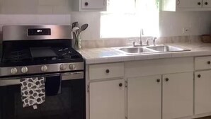 A kitchen with white cabinets, a stainless steel stove, and a window with a green curtain. - Experience a spacious three-bedroom, two-bathroom villa on the lush Northside. (St Thomas)