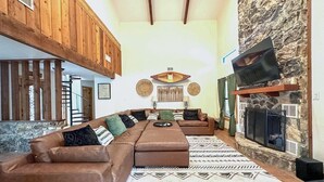 Un salon spacieux avec un grand canapé d’angle, une cheminée et un mur décoratif en pierre.