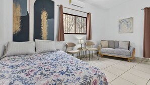Een slaapkamer met een groot bed, een bank, twee stoelen, een raam met gordijnen, een airconditioner en een schilderij aan de muur.