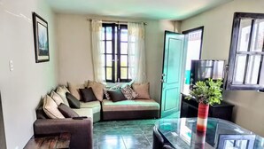 A living room with a glass table, black chairs, a sofa with patterned cushions, and a potted plant. - La Villa Playera. (Puerto Cayo)