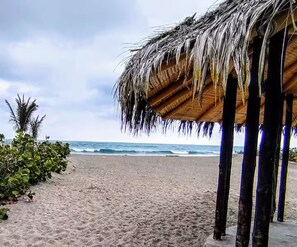 A beach with a thatched-roof structure, sandy beach, and ocean view. - La Villa Playera. (Puerto Cayo)