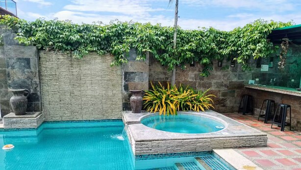 A swimming pool with a hot tub, stone walls, and a bar area with stools.