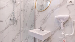 A bathroom with a glass-enclosed shower, a white sink, a hairdryer, and a marble wall.