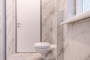 A bathroom with a toilet, marble walls, and a door.