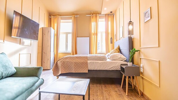 A modern hotel room with a bed, a sofa, a TV, and a small table.