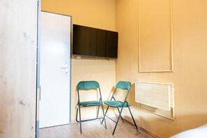 A room with a white door, two green chairs, a black TV mounted on the wall, and a wooden cabinet.