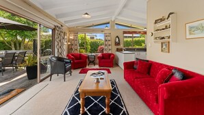 A modern living room with a red sofa, a wooden coffee table, and a glass door leading to an outdoor area. - Angela Close to the Lake (Taupo)