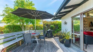 An outdoor deck with a table and chairs, a grill, and a large umbrella. - Angela Close to the Lake (Taupo)