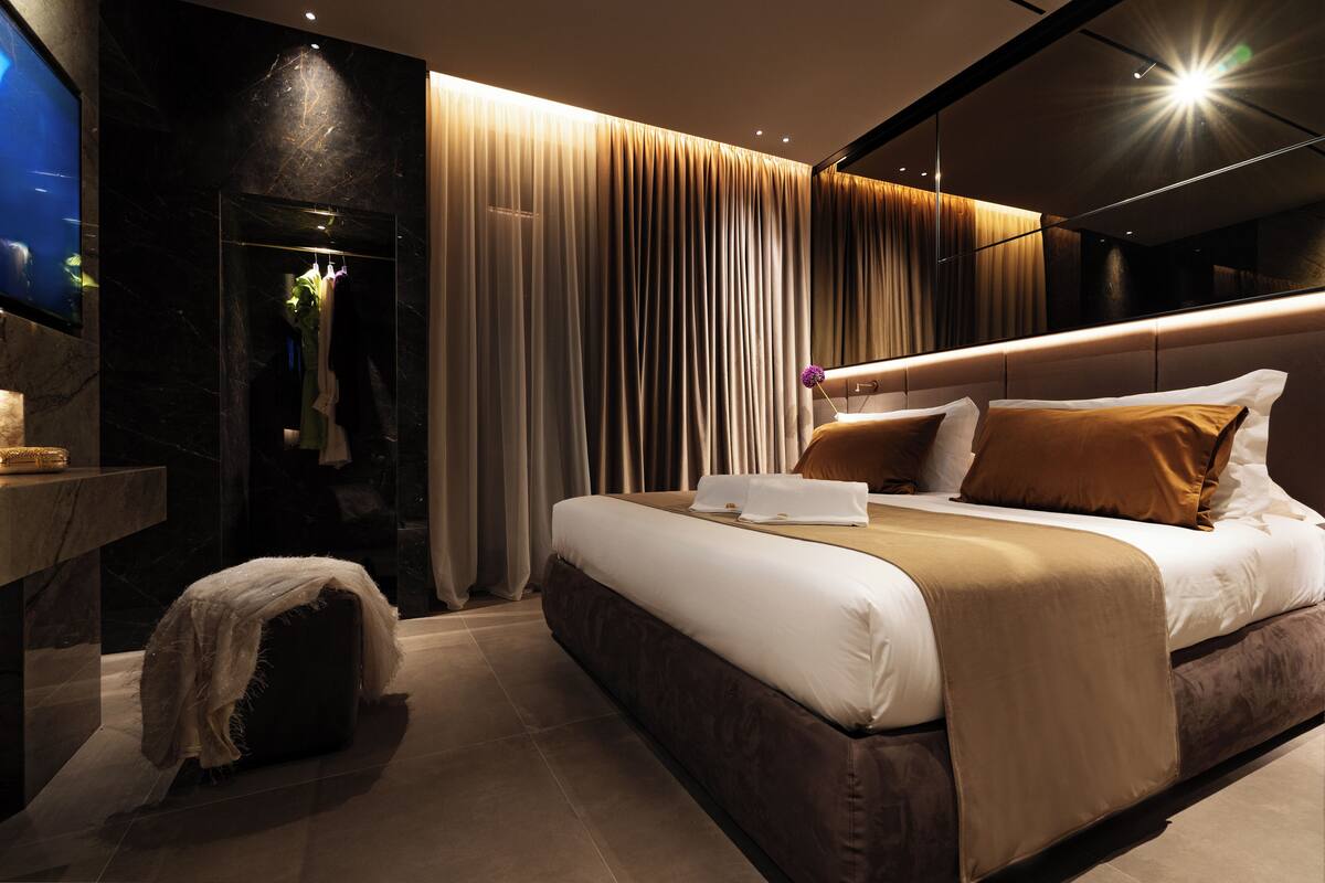 A modern hotel room with a large bed, a vanity with a mirror, and a television.