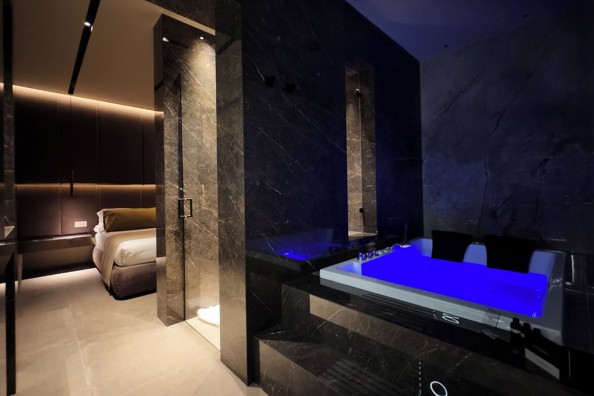 A modern bathroom with a large bathtub, marble walls, and a separate seating area.