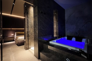 A modern bathroom with a large bathtub, marble walls, and a separate seating area.