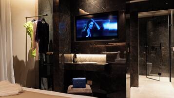 A modern bathroom with a large mirror, a flat-screen TV, a sink, and a shower area.