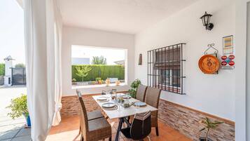 Comedor con una mesa preparada para cuatro personas, sillas de mimbre, una planta en maceta y vistas al exterior.