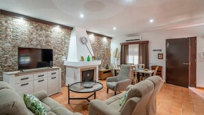 Un salon avec un mur en pierre, un téléviseur à écran plat, une cheminée, un coin repas et une porte.
