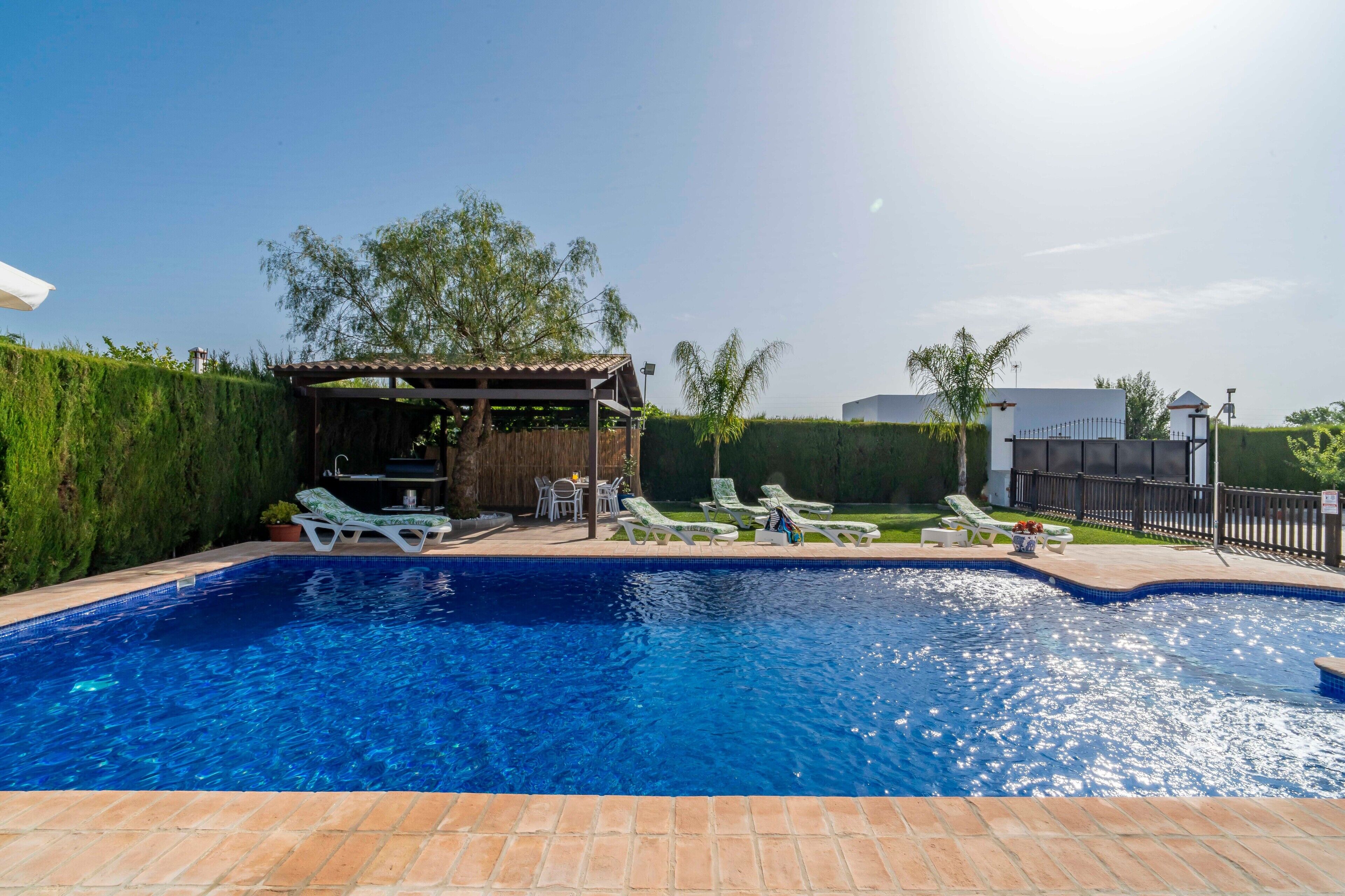 A swimming pool with lounge chairs, a pergola, and a fenced area.