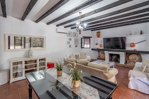 A living room with a sofa, a TV, a fireplace, and a ceiling with exposed beams.