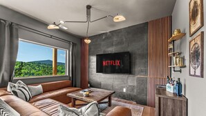 A modern living room with a leather sofa, a wooden coffee table, and a TV mounted on the wall. - Golden Heights - Sauna + 180 Degree Views + Hot Tub (Cripple Creek)