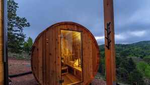 A wooden cabin with a glass door, interior lighting, and a view of a forested landscape. - Golden Heights - Sauna + 180 Degree Views + Hot Tub (Cripple Creek)