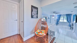 A spacious room with a white door, a colorful chair, a framed artwork, and a view of the outside through a window.