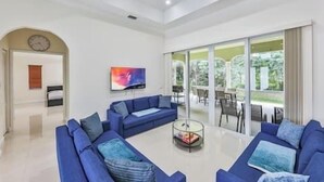 Ein geräumiges Wohnzimmer mit blauen Sofas, einem Couchtisch und einem großen Fenster mit Blick ins Freie.