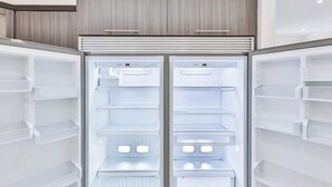 Ein moderner, leerer Kühlschrank mit mehreren Ablagen und Fächern, eingebettet in eine Küche mit Holzschränken.