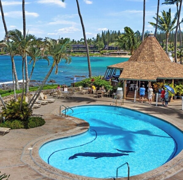 A pool with a dolphin design, surrounded by palm trees and a view of the ocean.