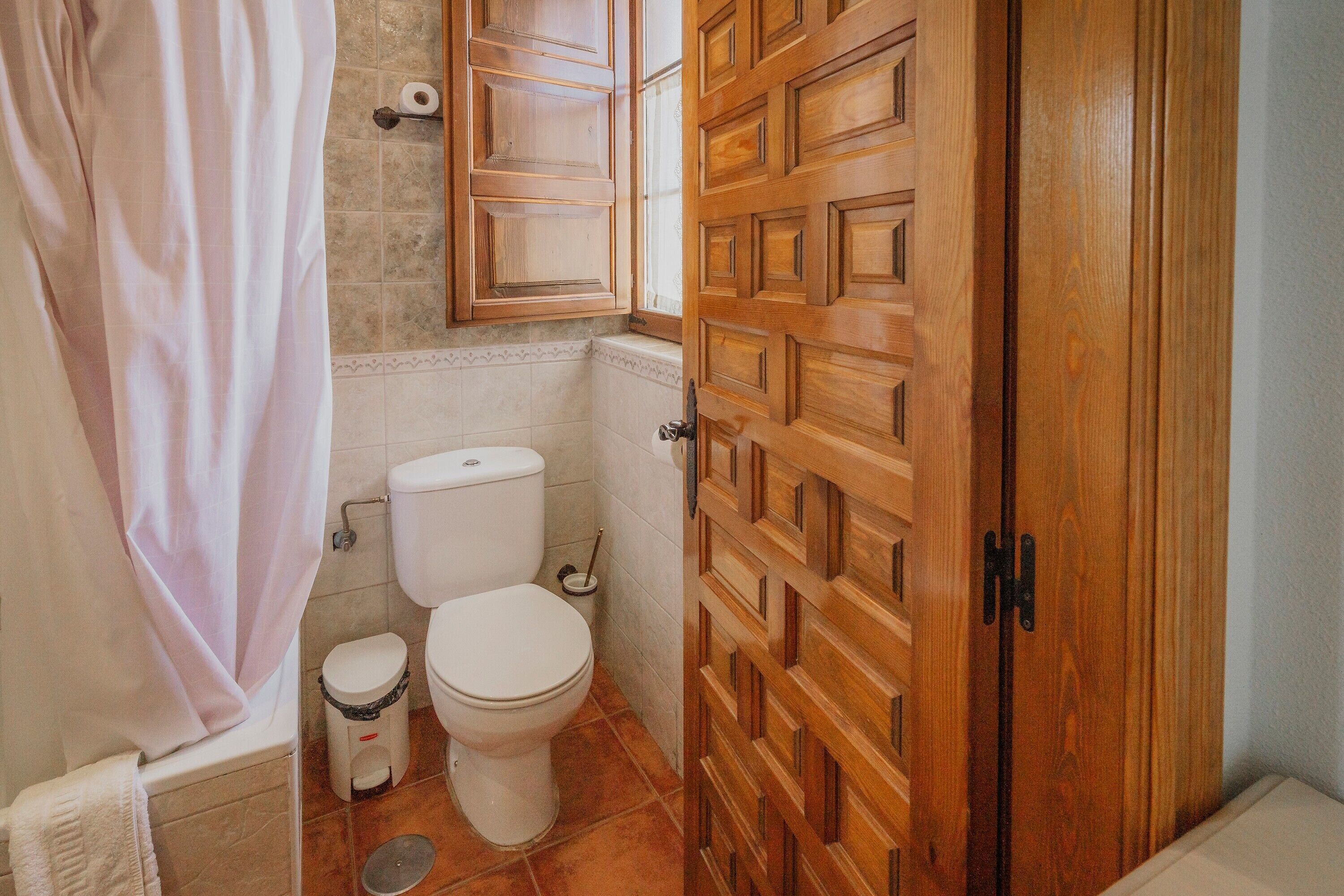 Un baño con inodoro, cortina de ducha, puerta de madera y ventana.