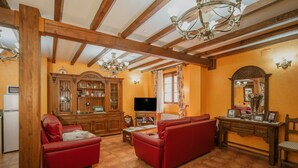 A living room with wooden beams, a television, red sofas, and a cabinet with glass doors.