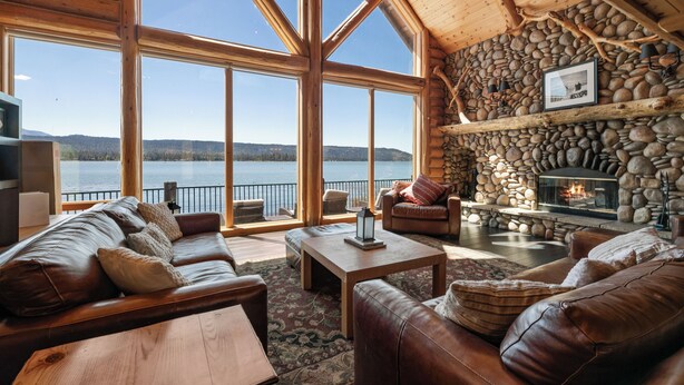 A log cabin interior with a stone fireplace, leather sofas, and large windows overlooking a lake. - Northern Exposure Lakefront (Fawnskin)