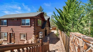 A log cabin with a stone wall and wooden fence, surrounded by greenery. - Northern Exposure Lakefront (Fawnskin)
