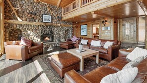 A log cabin interior with a stone fireplace, leather furniture, and a wooden balcony. - Northern Exposure Lakefront (Fawnskin)