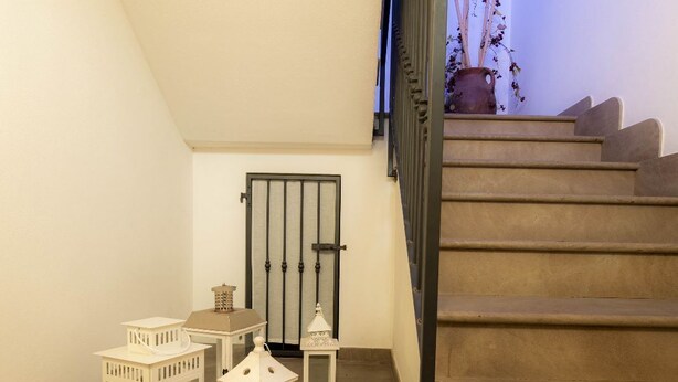 A staircase with beige steps and a wooden handrail, leading to a landing with a metal gate and a potted plant.